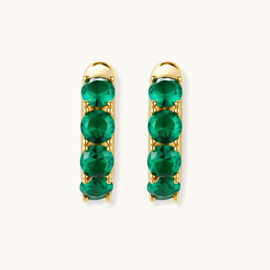 Close-up of gold-plated huggie hoop earrings featuring four emerald green cubic zirconia stones on white background.
