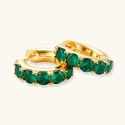 Close-up of gold-plated huggie hoop earrings featuring four emerald green cubic zirconia stones on white background.