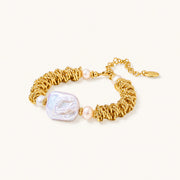 18k gold-plated bracelet with textured wave segments, baroque pearl centerpiece, and round freshwater pearls on cream background