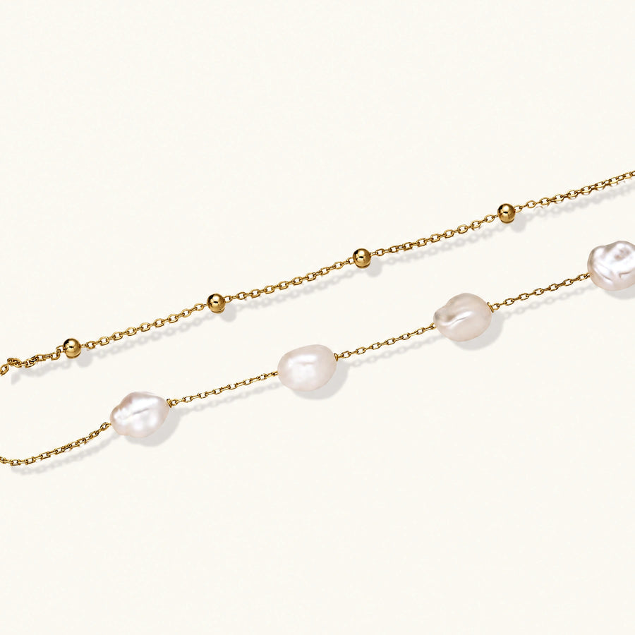 Double-strand gold bracelet with irregular baroque pearls and smooth freshwater pearls on cream background.