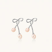 Rhodium-plated silver earrings with organic vine curves and two peachy freshwater pearls on cream background