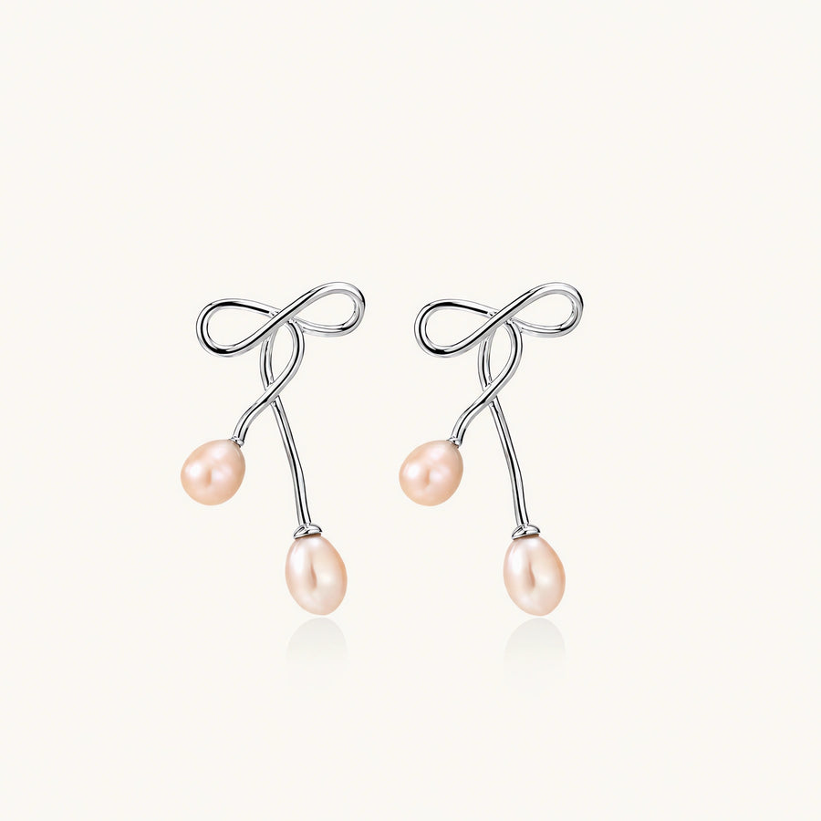 Rhodium-plated silver earrings with organic vine curves and two peachy freshwater pearls on cream background