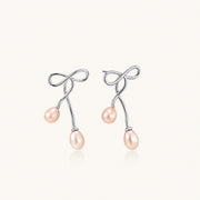 Rhodium-plated silver earrings with organic vine curves and two peachy freshwater pearls on cream background