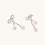 Rhodium-plated silver earrings with organic vine curves and two peachy freshwater pearls on cream background