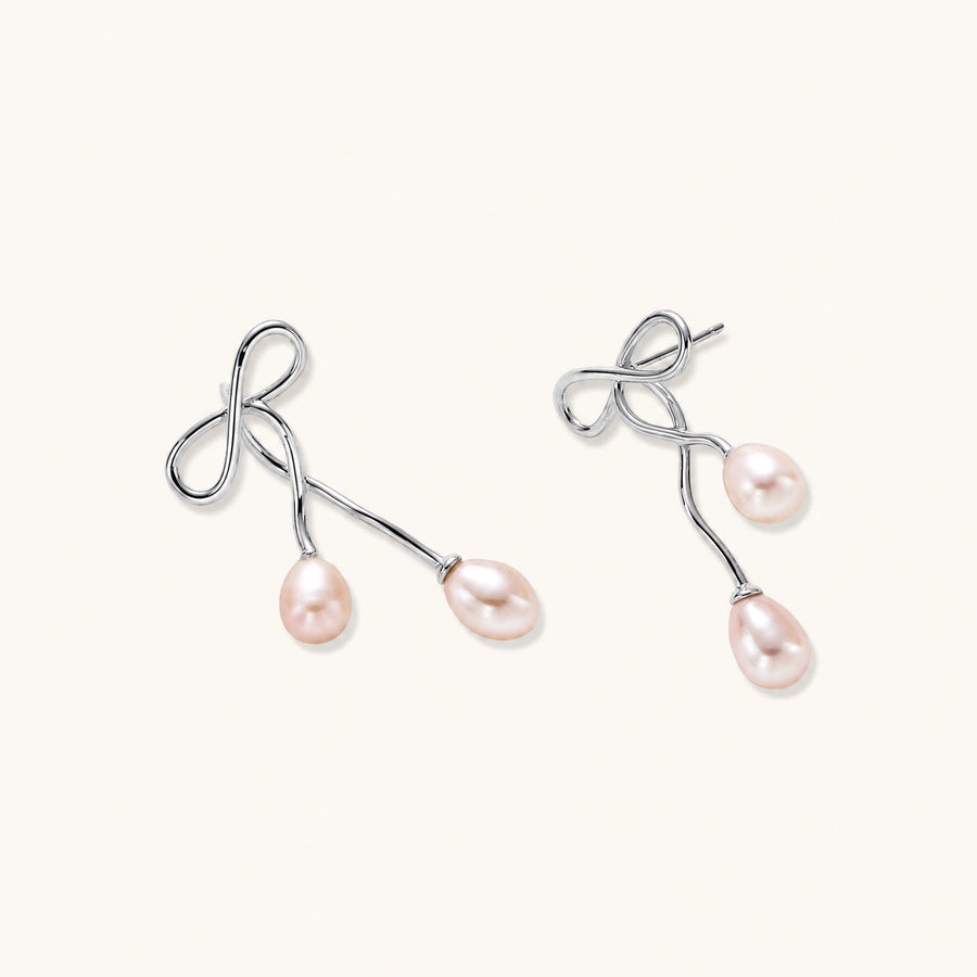 Rhodium-plated silver earrings with organic vine curves and two peachy freshwater pearls on cream background