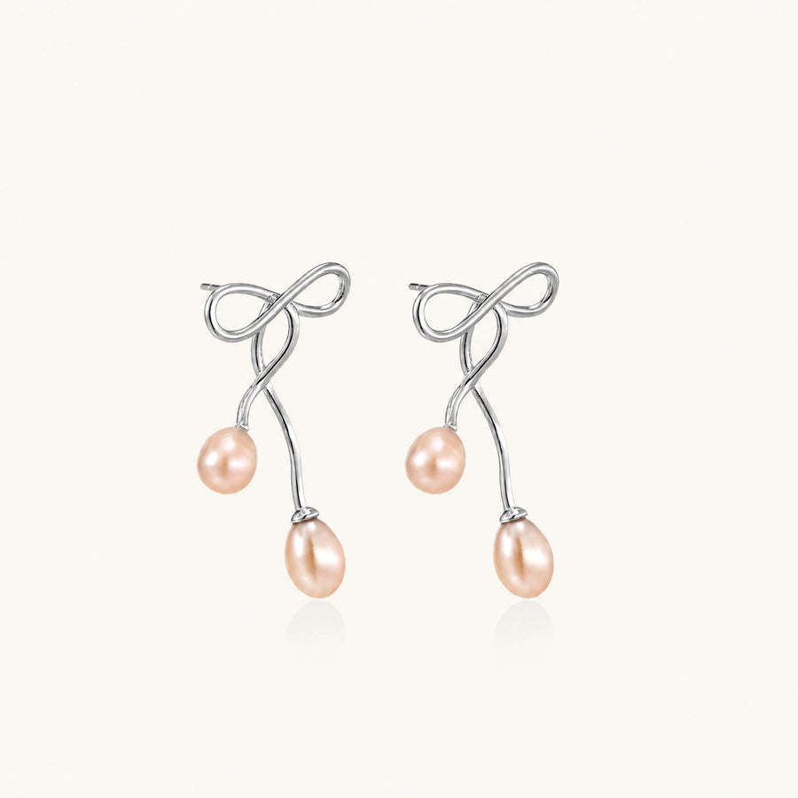 Rhodium-plated silver earrings with organic vine curves and two peachy freshwater pearls on cream background