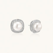 Rhodium-plated sterling silver stud earrings with round freshwater pearls surrounded by geometric crystal halos on cream background.