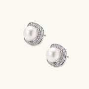 Rhodium-plated sterling silver stud earrings with round freshwater pearls surrounded by geometric crystal halos on cream background.