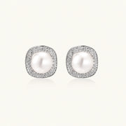 Rhodium-plated sterling silver stud earrings with round freshwater pearls surrounded by geometric crystal halos on cream background.