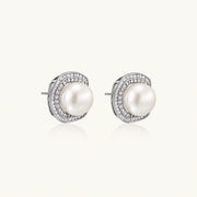 Rhodium-plated sterling silver stud earrings with round freshwater pearls surrounded by geometric crystal halos on cream background.