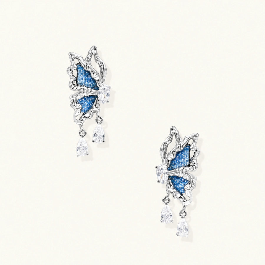 Silver butterfly earrings with blue denim fabric wings and dangling teardrop crystals on cream background