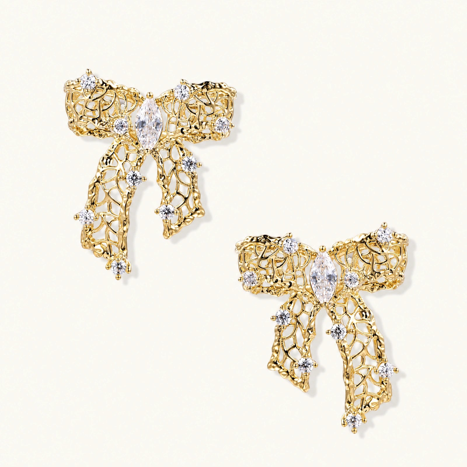 Gold-plated bow earrings with openwork design, marquise center stones, and flowing ribbon tails adorned with zirconia crystals.