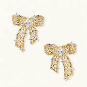 Gold-plated bow earrings with openwork design, marquise center stones, and flowing ribbon tails adorned with zirconia crystals.