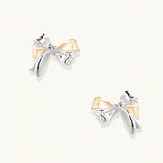 Pair of bow stud earrings with mirror-finish silver-tone ribbons and cream enamel-look loops on a cream background.