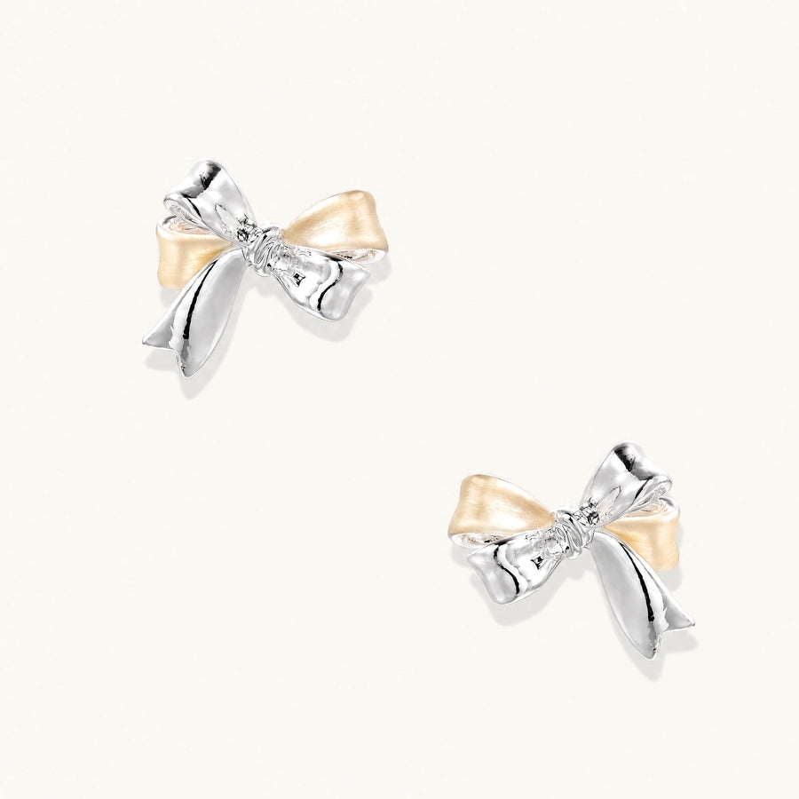 Pair of bow stud earrings with mirror-finish silver-tone ribbons and cream enamel-look loops on a cream background.