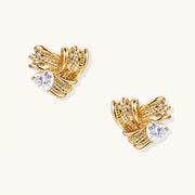 Pair of sculptural gold-plated wing stud earrings with zirconia stones on cream background, showing dimensional feather design