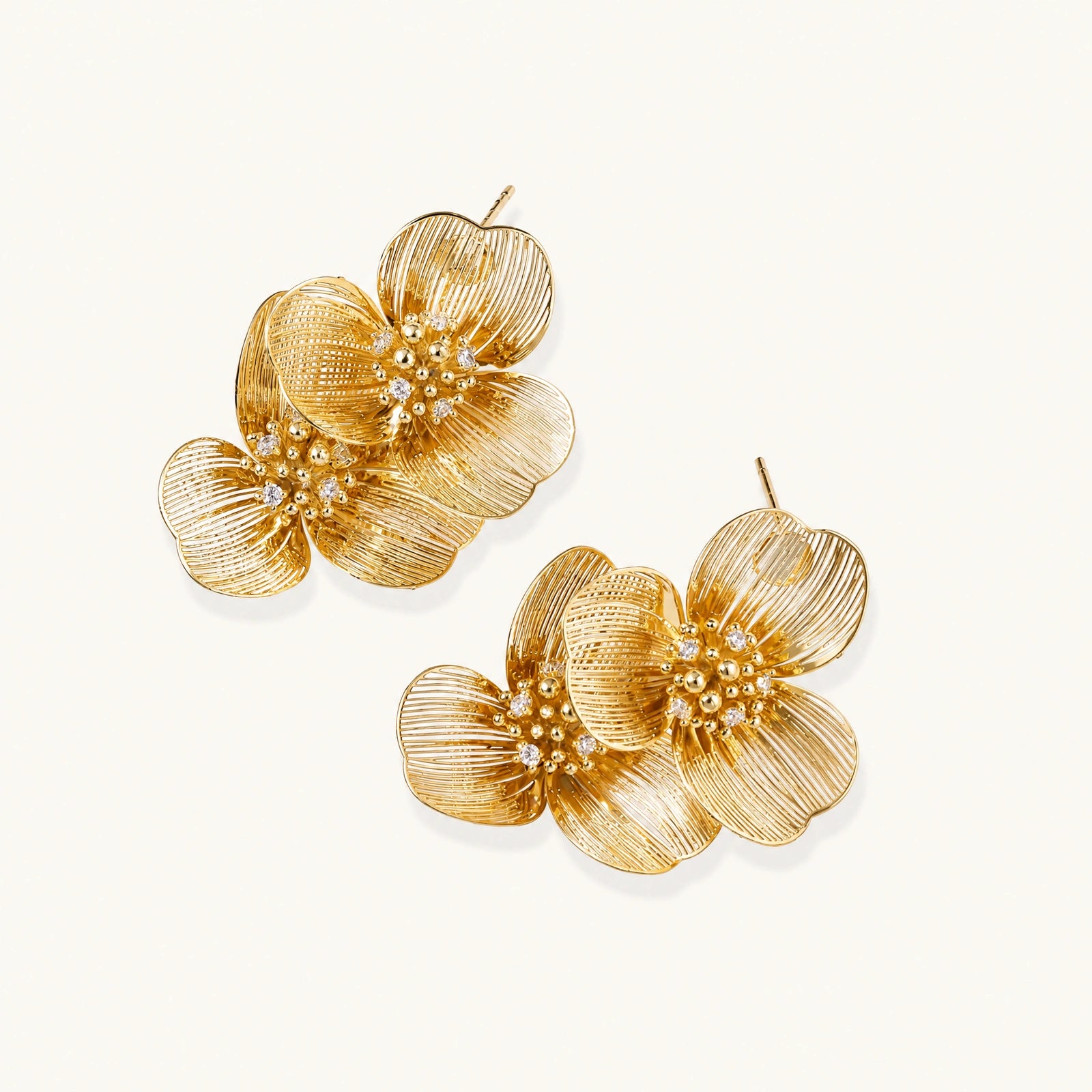 Pair of gold-plated double flower earrings with textured petals and crystal centers on cream background.