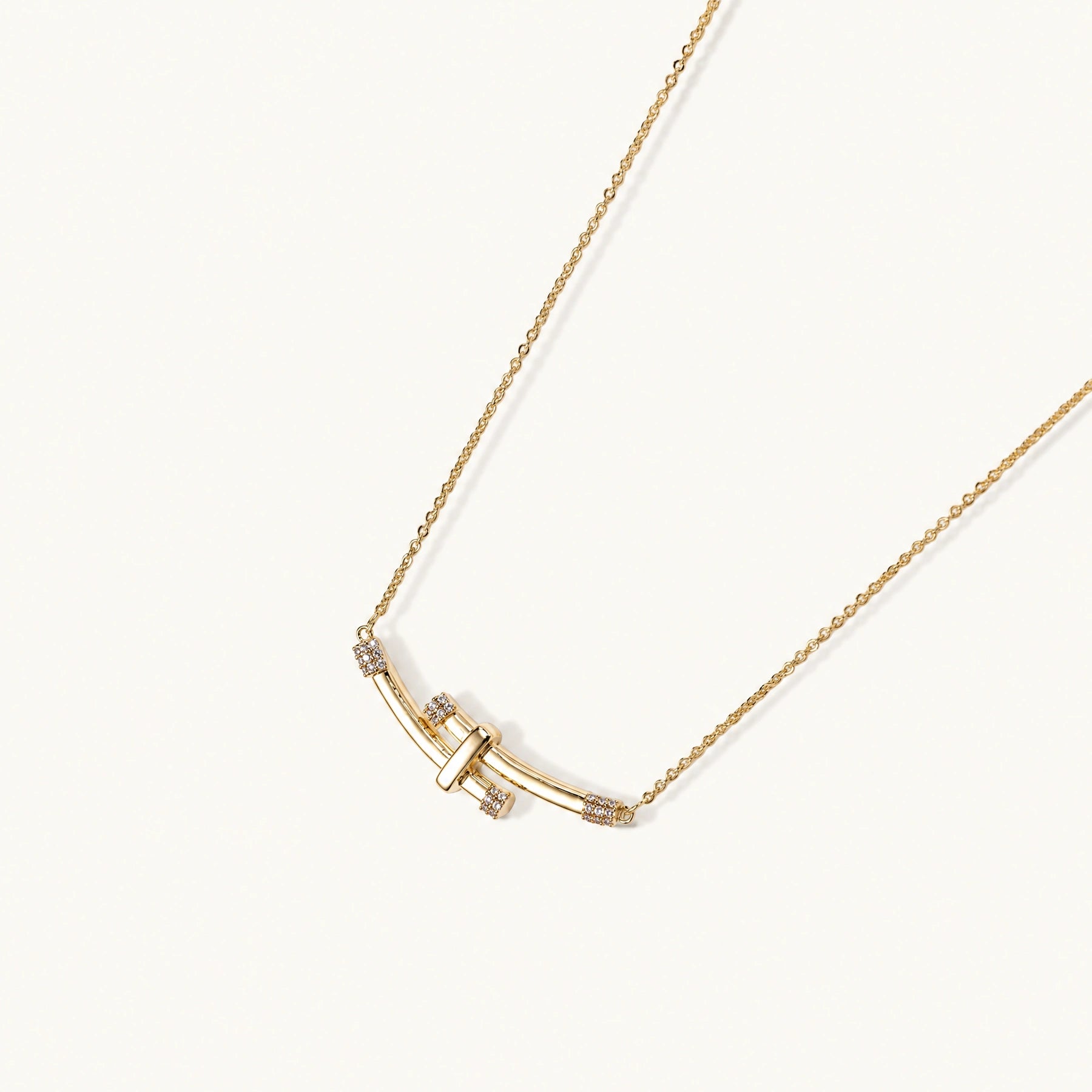 Gold-plated curved bar necklace with diamond accents on delicate chain against cream background