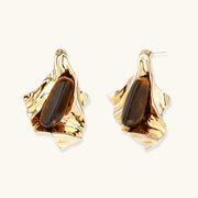 Sculptural gold-tone earrings with flowing organic forms and amber gemstone accents on neutral background