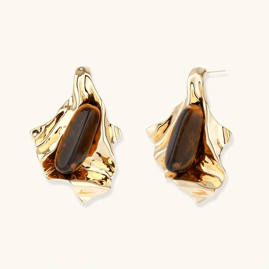 Sculptural gold-tone earrings with flowing organic forms and amber gemstone accents on neutral background