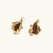 Sculptural gold-tone earrings with flowing organic forms and amber gemstone accents on neutral background