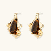Sculptural gold-tone earrings with flowing organic forms and amber gemstone accents on neutral background