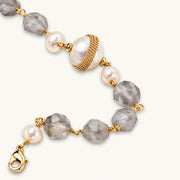 Bracelet with cloudy quartz beads, freshwater pearls, and gold-wrapped baroque pearl centerpiece on white background.