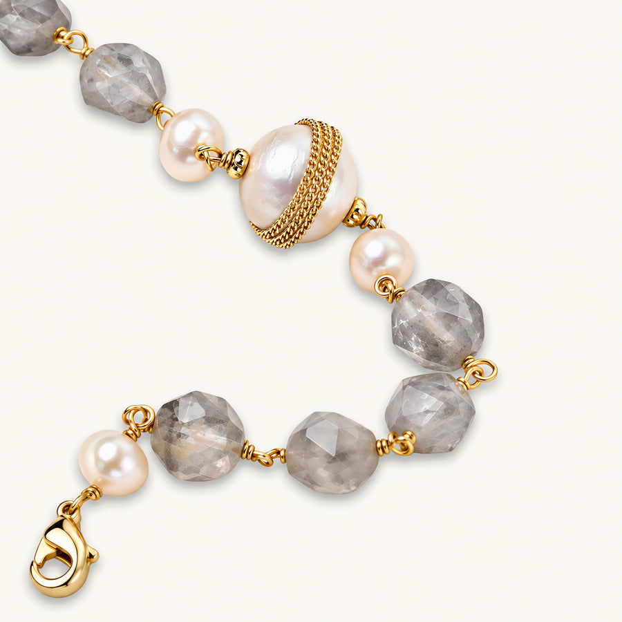 Bracelet with cloudy quartz beads, freshwater pearls, and gold-wrapped baroque pearl centerpiece on white background.
