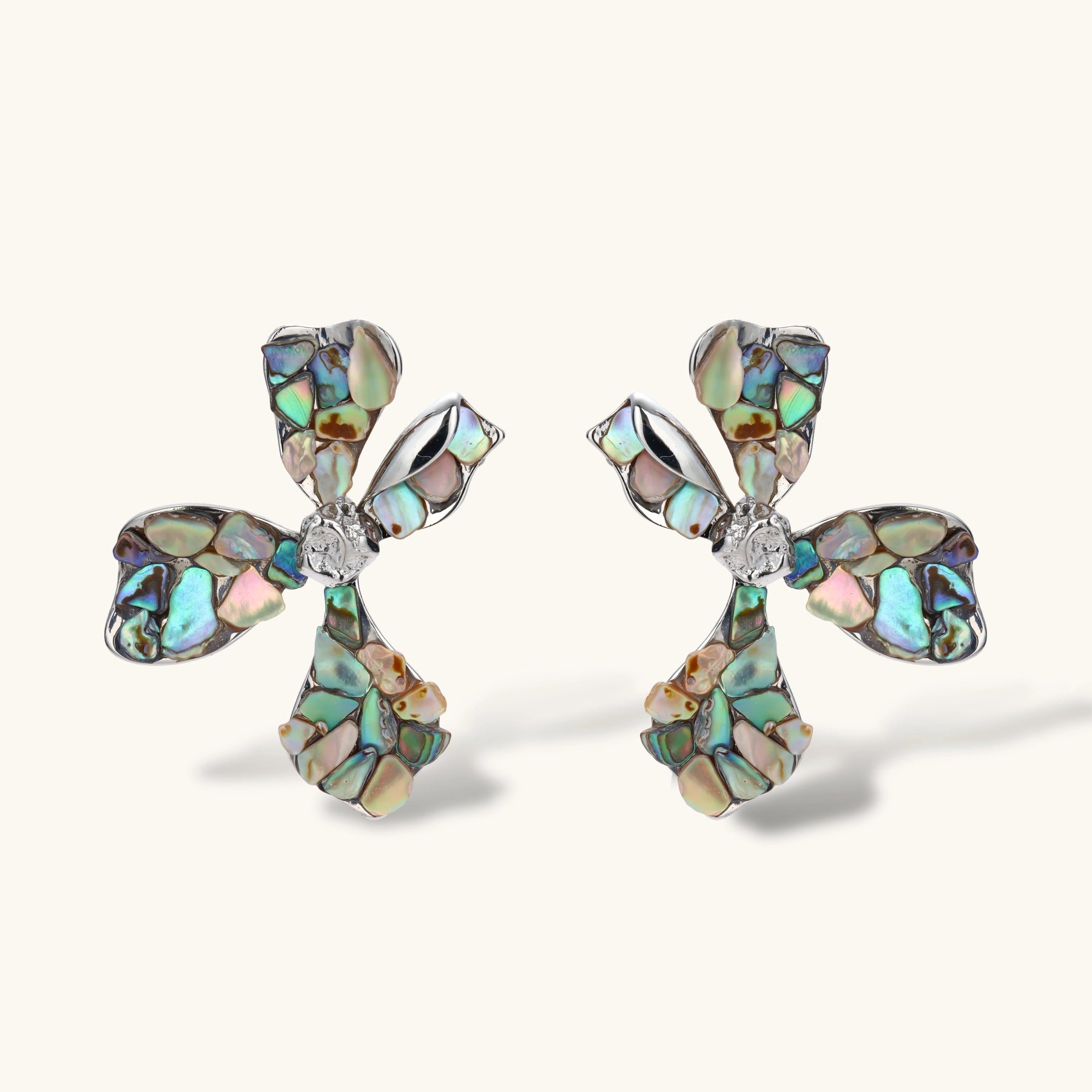 Pair of oversized four-petal flower stud earrings with iridescent teal and blush shell mosaic on silver-tone petals.