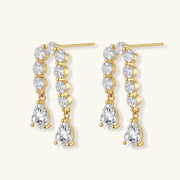 Gold-plated earrings with vertical line of clear crystals and teardrop pendants on neutral background