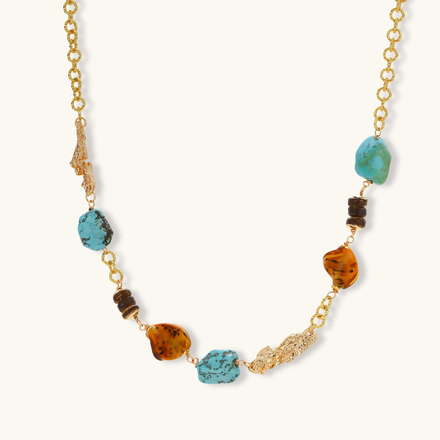 Gold plated eco-brass chain necklace with turquoise nuggets, amber-toned stones, brown discs and molten gold accents on cream.